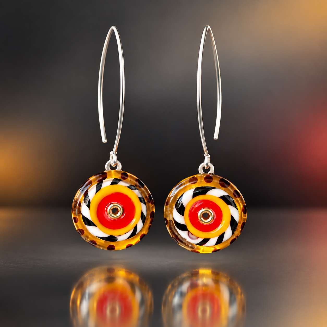 Handmade graphic lampwork glass dangle earrings with concentric red and yellow circles, black and white swirls, amber accents, stainless steel settings, and long sterling silver fishhook ear wires.